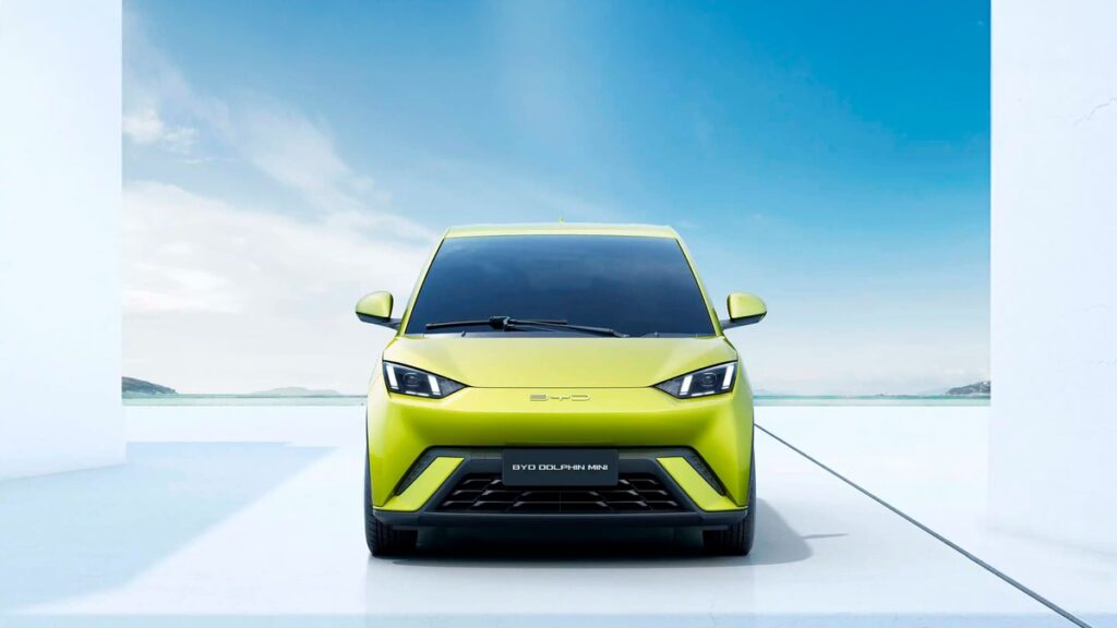 Frente do BYD Dolphin Mini em cor verde-limão estacionado em cenário moderno ao ar livre, destacado sob céu azul.