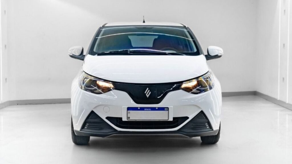 Visão frontal direta do JMEV Emova Easy, o carro elétrico mais barato do Brasil, destacando seus faróis acesos, grade preta integrada com o logotipo central e placa padrão Mercosul em um estúdio branco.
