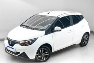 Visão em ângulo de três quartos da dianteira do JMEV Emova Easy, o carro elétrico mais barato do Brasil, um hatch compacto urbano com carroceria em dois tons (teto preto e pintura clara) posicionado em um estúdio fotográfico moderno.