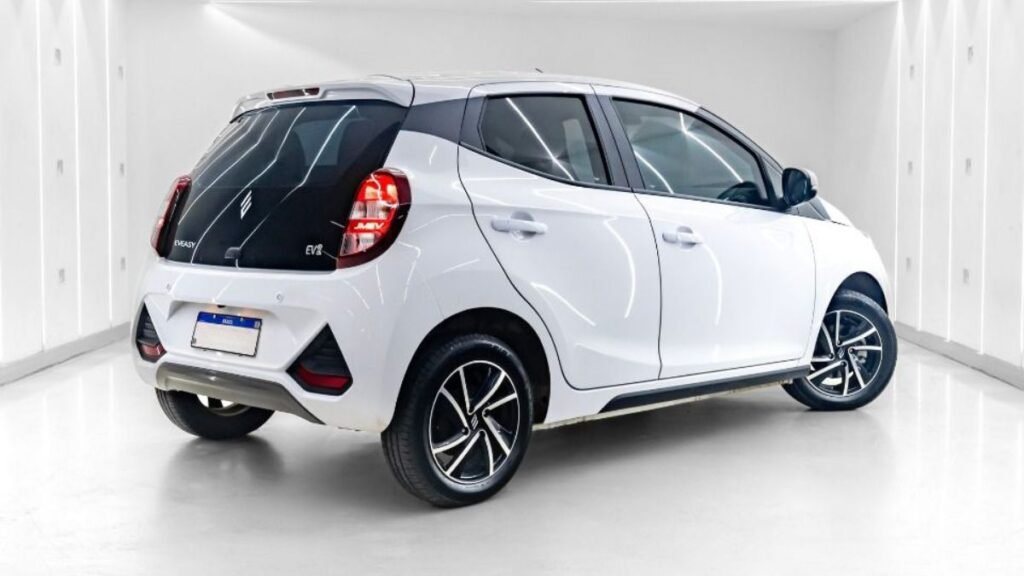 Visão em ângulo de três quartos da traseira do JMEV Emova Easy, o carro elétrico mais barato do Brasil, destacando a tampa do porta-malas em vidro preto com lanternas verticais acesas e para-choque branco em um estúdio fotográfico iluminado.