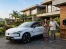 Fotografia de um SUV elétrico Volvo EX30 branco estacionado na rampa de uma casa moderna de alto padrão enquanto carrega em um carregador de parede (wallbox). Ao lado do carro, um casal sorri e conversa, ilustrando a rotina de quem aproveita as vantagens do IPVA Carro Elétrico MG.