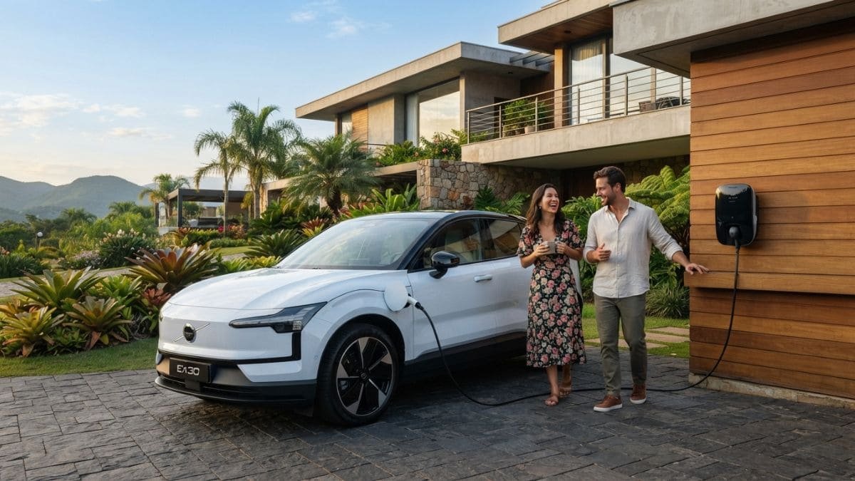Fotografia de um SUV elétrico Volvo EX30 branco estacionado na rampa de uma casa moderna de alto padrão enquanto carrega em um carregador de parede (wallbox). Ao lado do carro, um casal sorri e conversa, ilustrando a rotina de quem aproveita as vantagens do IPVA Carro Elétrico MG.