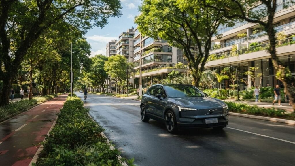 Fotografia em plano médio de um SUV elétrico Volvo EX30 cinza em movimento por uma avenida urbana densamente arborizada. Ao fundo, destacam-se edifícios residenciais modernos com varandas repletas de plantas e uma ciclovia na lateral, representando a mobilidade sustentável associada ao IPVA Carro Elétrico Paraná.